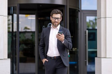 Sakallı, olgun bir iş adamı. Telefonunda modern ofis binasının dışındaki güncellemeleri kontrol ediyor. Başarıyı resmediyor..