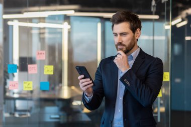 Düşünceli, olgun bir iş adamı. Arkasında notlar olan akıllı bir telefon kullanıyor. Stratejik düşünme tarzını yansıtıyor..