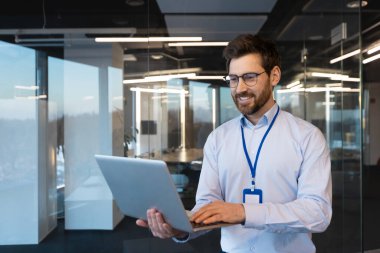 Çağdaş ofiste dizüstü bilgisayar kullanarak gülümseyen olgun erkek profesyonel liderlik ve uzmanlığı somutlaştırıyor..