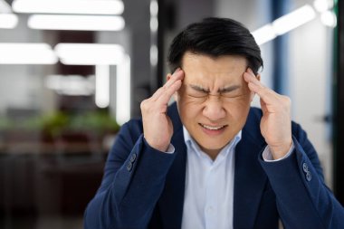 Ofisin içinde bir adamın başı ağrıyor, takım elbiseli Asyalı bir iş adamı hasta, migreni var, patron elinde dizüstü bilgisayarla bir masada oturuyor..