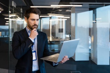 Olgun, ciddi görünümlü bir iş adamı, liderliği ve stratejik düşünceyi temsil eden, düzgün, çağdaş bir ofis ortamında, bilgisayarındaki verileri analiz eder..