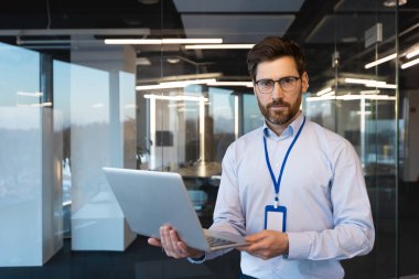 Çağdaş bir ofisin içinde dizüstü bilgisayarda çalışan akıllı bir iş adamı liderlik ve kararlılık yayıyor..