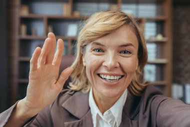Sarışın, neşeli, olgun bir kadın ev ofisinden merhaba diyor, profesyonelliği ve arkadaşlığı simgeliyor..