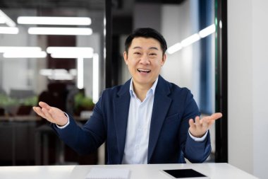 Takım elbiseli Asyalı işadamı bir konsepti açıklarken ya da modern ofis ortamında sunum yaparken.