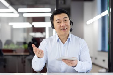 Ofis ortamında kulaklık takmış gülümseyen erkek müşteri hizmetleri acentesi müşterilere coşku ve profesyonellikle yardım ediyor..