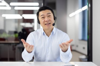 Webcam görüntüsü, kulaklık takan Asyalı destek görevlisi gülümseyen ve kameraya bakan iş adamı ofis içi çalışan, müşterilere uzaktan danışan, iş arkadaşlarıyla uzaktan görüşen..