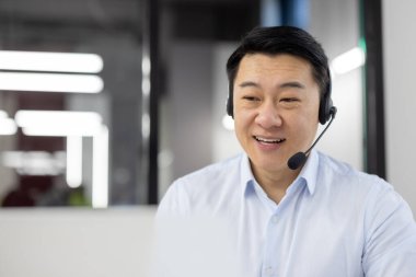 Ofisin içinde kulaklıklı bir adam, gömlek giyen Asyalı bir müşteri hizmetleri çalışanı, video görüşmesi için laptop kullanan bir iş adamı ve müşteri danışmanlığı, telefon satışları.,