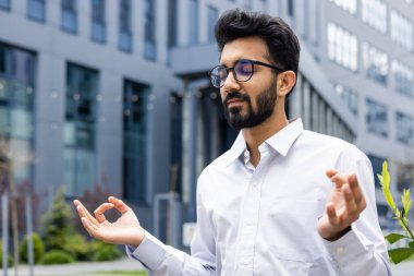 Genç bir şirket çalışanı molada dinleniyor, gömlekli bir işadamı, meditasyon yapıyor, gözleri lotus pozisyonunda kapalı oturuyor, rahatlıyor ve düşünüyor..