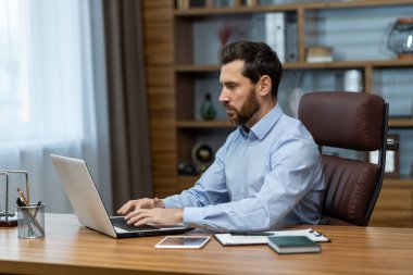 Odaklanmış ve ciddi bir genç adam ofiste bir proje üzerinde çalışıyor, veri ve bilgileri kopyalayıp analiz ediyor..