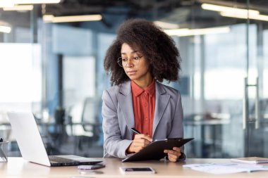 Yuvarlak gözlüklü kadın ofis içi yazı tahtasına döküman doldururken bilgisayar ekranına bakıyor. E- postadan basılı kağıtlara bilgi kopyalayan kendine güvenen girişimci.