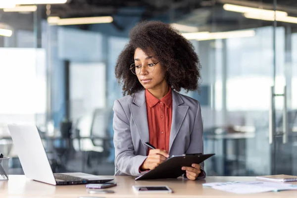 Yuvarlak gözlüklü kadın ofis içi yazı tahtasına döküman doldururken bilgisayar ekranına bakıyor. E- postadan basılı kağıtlara bilgi kopyalayan kendine güvenen girişimci.