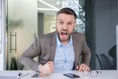 Öfkeli bir ofis çalışanı yumruklarını sıkarak bağırıyor. Güçlü duygular ve işyeri stresi gösteriyor. Şirket içi arka planına karşı..