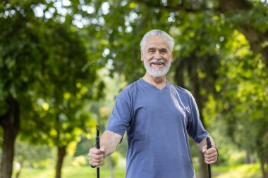 Neşeli yaşlı beyefendi yürüyüş çubuklarıyla dışarıda spor yapmayı seviyor, refah ve sağlıklı yaşam tarzını ifade ediyor..
