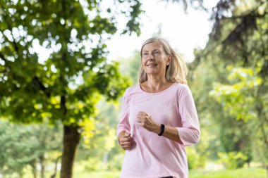 Aktif, yeşil bir parkta koşan gülümseyen ve altın yıllardaki sağlık ve zindeliği kucaklayan son sınıf öğrencisi bir kadın..