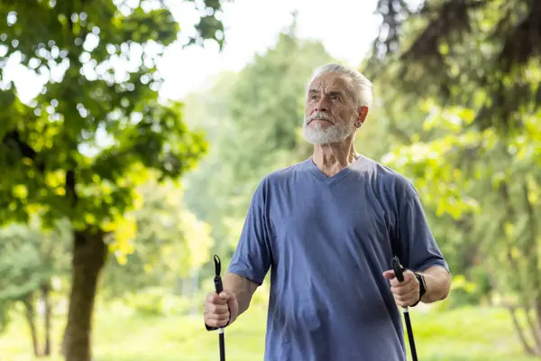 An active elderly man with trekking poles walks in a serene park, showcasing fitness and enjoyment of nature.