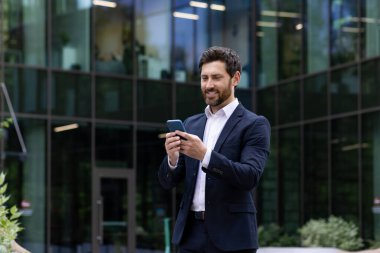 Terzi kıyafetli profesyonel bir adam dışarıda mola verip telefonuna mutlu bir gülümsemeyle bakmaktan hoşlanır..