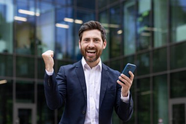 Şen şakrak iş adamı modern şehir ofisinin cam cephesinin dışında zafer yumruğu sallıyor..