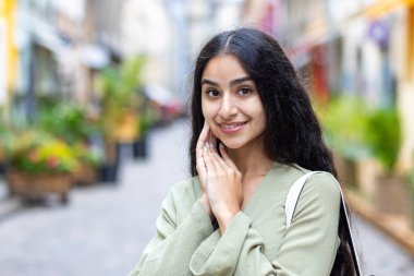 Şehir sokaklarında elini yüzüne dayayıp kameraya poz veren yeşil takım elbiseli güzel bir Hintli kızın yakın plan fotoğrafı..