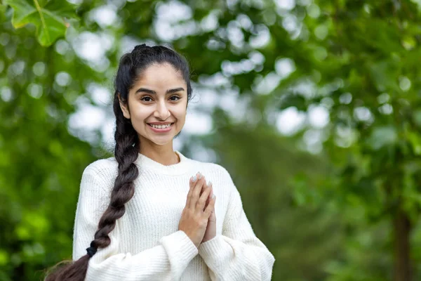 Portrait of an Indian beautiful smiling woman standing in a park with her arms folded and looking at the camera in casual sportswear. Close-up photo.