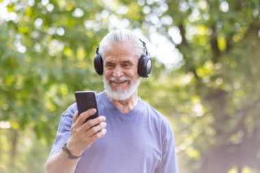 Dışarıda kulaklık takan neşeli, yaşlı bir beyefendi. Etkin kıdemli yaşam tarzı ve teknoloji kullanımını vurgular.