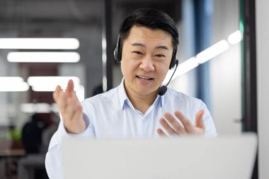 Kablosuz kulaklıklı, bilgisayar ekranına bakan ve esprili elleri olan dost canlısı bir destek yöneticisi. Japon işçiler video toplantısına katılıyor ve en son başarılar hakkında rapor hazırlıyorlar..