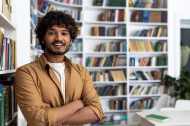 Dolu bir kütüphanede kollarını kavuşturmuş kendinden emin bir gencin portresi. Resim, bir kitaplık arkaplan arasında bilgi, eğitim ve kendine güven duygusu aktarıyor