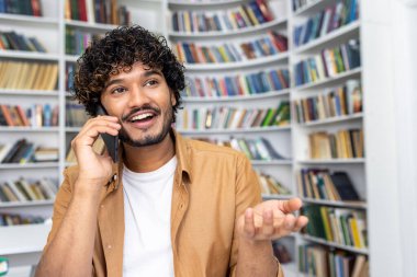 Sıradan kıyafetli bir adam, iyi aydınlatılmış bir kütüphane ortamında kitaplıklarla dolu kitaplıklarla çevrili bir telefon görüşmesindedir. Bu kavram iletişimi ve öğrenmeyi yakalar.