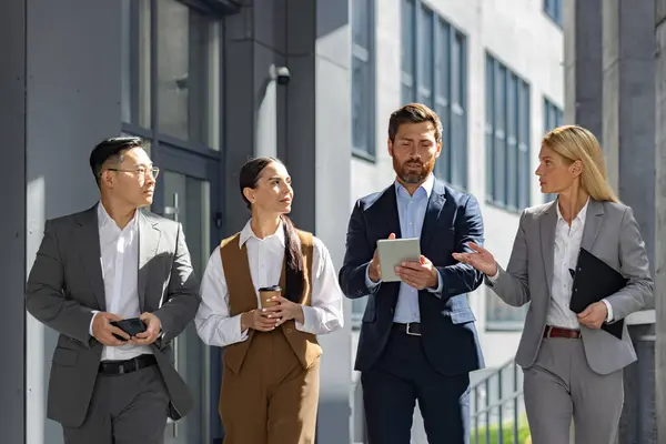 A dynamic group of business professionals is captured mid-conversation outside a modern office building, reflecting teamwork, strategy, and corporate engagement.