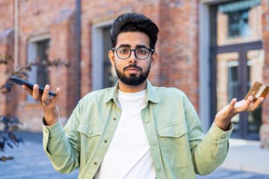 Gözlüklü belirsiz bir adamın portresi modern akıllı telefonu dışarıda tutarken karmaşa içinde el sallıyor. Mutsuz erkek, teknik problemleri olan aletlerle bağlantıyı kaybetmekten memnun değil..