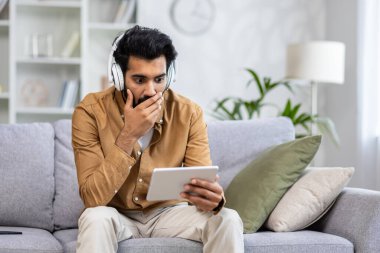 Beyaz kulaklıklı, şok olmuş Müslüman adam oturma odasında dijital tablet ekrana bakarken ağzını eliyle kapatıyor. İnanılmaz bir adam korku filmi izler ve destansı anlardan etkilenir..