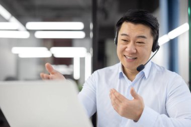 Kulaklıklı neşeli Asyalı işadamı bir video çağrısında el hareketleriyle konsepti açıklıyor..