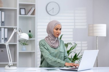 İyi aydınlatılmış, modern ofis ortamında tesettürlü, tesettürlü, tesettürlü Müslüman bir kadın temiz bir tasarıma sahip..