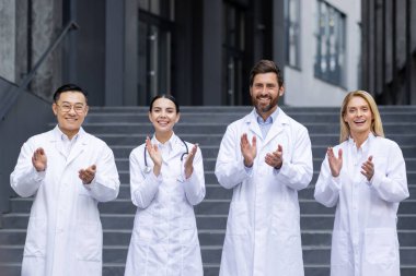 Kliniğin önünde beyaz önlüklü, kameraya bakıp alkışlayan ve gülümseyen bir grup doktorun portresi..