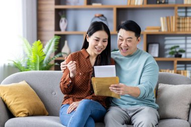 Mutlu Asyalı çift evdeki kanepede oturmuş, bir mektupla gelen güzel haberi kutluyorlar..