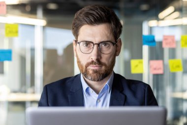 Modern ofis ortamında renkli yapışkan notlarla çevrili bir dizüstü bilgisayar üzerinde odaklanmış bir profesyonel..