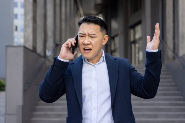 Stresli bir telefon üzerine sinirli bir yönetici şehir merkezinde ofis binalarının önünde dikilirken hayal kırıklığını ifade ediyor..