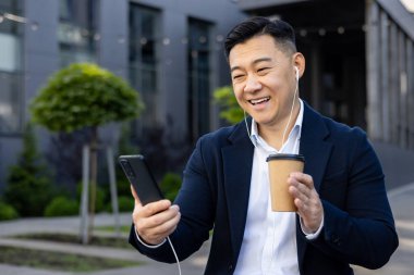 Takım elbiseli mutlu bir yönetici rahatlatıcı bir kahve molası sırasında telefonundan müzik dinliyor..