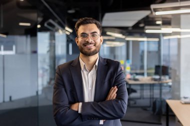 Profesyonel bir işadamı kollarını kavuşturup modern ofis ortamlarına güvenir..