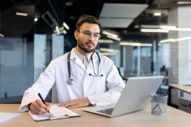 Parlak çağdaş bir tıp ofisinde bilgisayar kullanırken odaklanmış sağlık hizmeti uzmanı notları. Modern tıp ve sağlık hizmetleri kavramı.