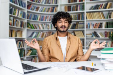 Orta Doğulu adam bilgisayarının başında oturuyor ve Gyan Mudra 'da gözleri kapalı ellerini kaldırıyor. Yoga pozu kullanan sakin programcı stresten kurtulmak ve zihni özgür kılmak için pratik yapıyor..