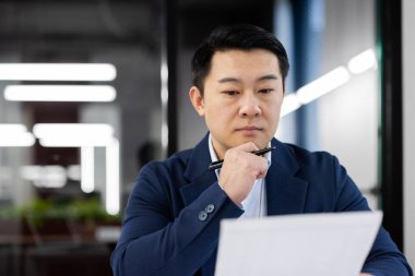 Profesyonel Asyalı işadamı modern ofis ortamında yoğunlaşarak evrak işlerini inceliyor..