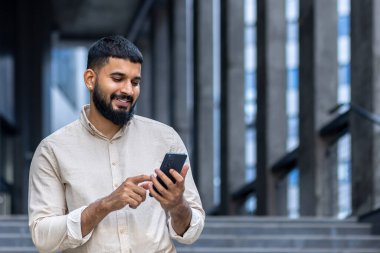 Sakallı neşeli genç bir adam şehir merdivenlerinde akıllı telefonuyla meşgul. Görüntü modern bağlantıyı ve şehir yaşam tarzını tasvir ediyor, her gün bir neşe ve teknoloji kullanımı anı yakalıyor
