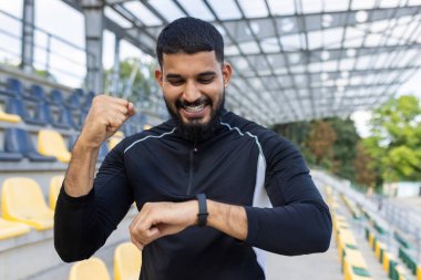 Spor kıyafetleri içinde sakallı bir genç, spor salonundaki bir yumruk pompasıyla fitness hedefini kutluyor..
