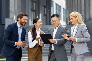 Resmi giyinmiş profesyonel bir iş ekibi modern bir ofis binasının önünde bir tartışmaya girişti..