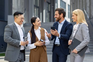 Dört gülümseyen iş adamı, modern bir şehir ortamında, tabletler ve akıllı telefonlar ile açık havada gündelik bir toplantı yapıyorlar..