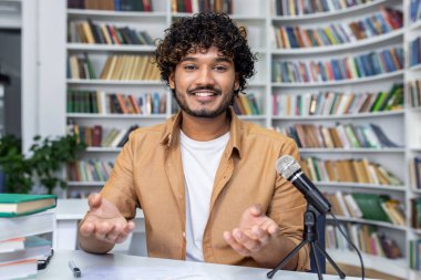 Kütüphanede arka planda mikrofon ve kitaplarla podcast kaydetmeye odaklanmış bir birey.