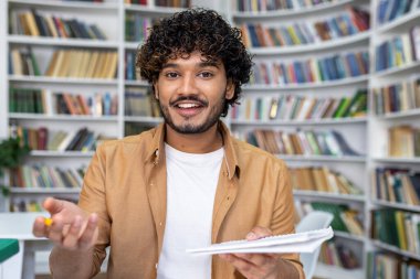Kıvırcık saçlı neşeli bir genç elinde bir defter tutuyor ve bilgi sunuyor, bir kitapçıda ya da kütüphanede gayri resmi bir toplantı ya da özel ders öneriyor..