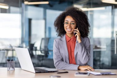 Genç profesyonel bir kadın ofis masasında teknoloji ve modern ofis dekorasyonu ile çevrili bir telefon görüşmesi yapıyor..