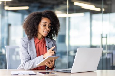 Genç bir iş kadını notlar alırken işine odaklandı ve modern ofis ortamında dizüstü bilgisayar kullandı..