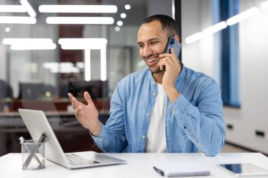 Neşeli iş adamı, modern bir ofis masasında, pozitiflik ve profesyonellik sergileyen telefon görüşmeleriyle meşgul..